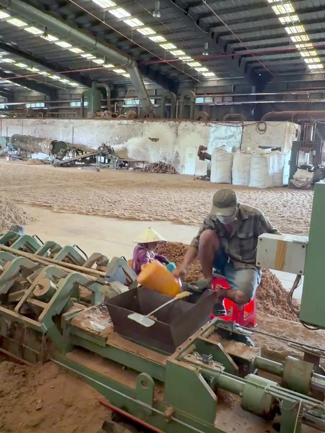 A worker loading coir into a large green press inside the workshop