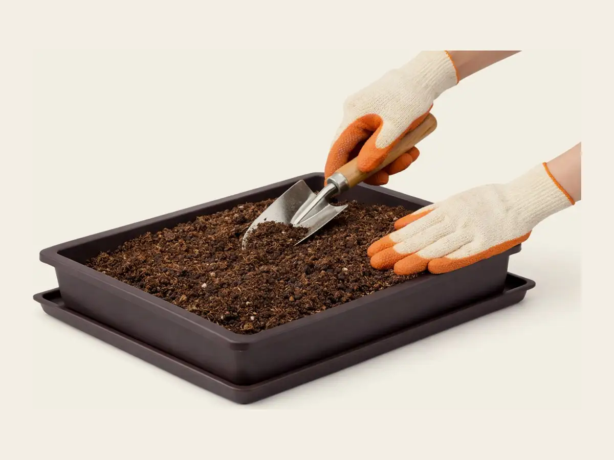 Gloved hands loosening expanded coir in a tray with a small trowel