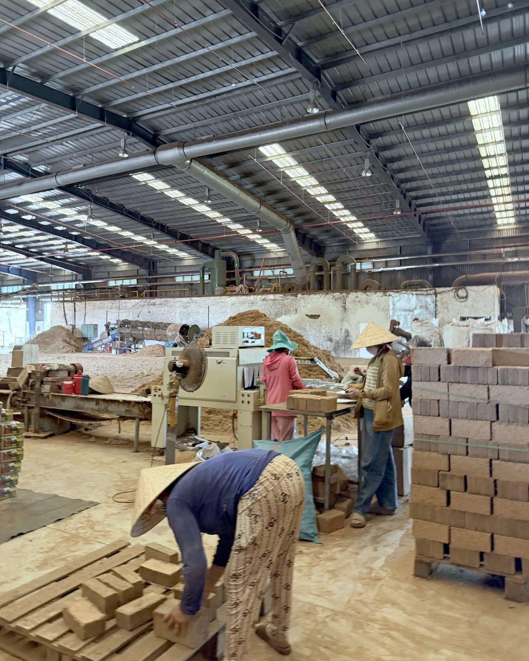 Workers stacking freshly pressed coir bricks beside the brick presses inside the Bến Tre workshop